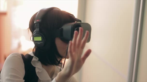 Young brunette woman playing game using VR-helmet for smart phones. Augmented reality device allows to deep into virtual space - Footage, Video
