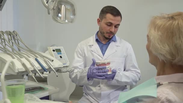 Dentist explaines something on layout of teeth to his female client - Πλάνα, βίντεο