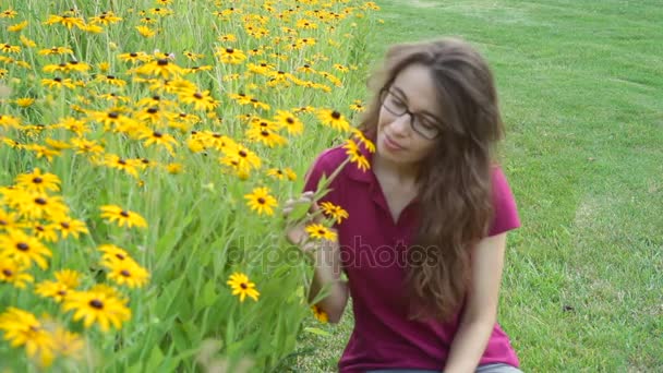 Cute young woman smelling yellow flowers on a flowerbed in the park - Footage, Video