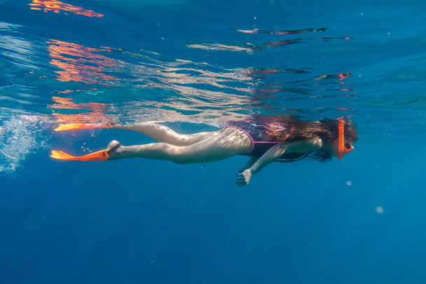 Girl in orange swimming mask and flippers dive in deep sea - 写真・画像