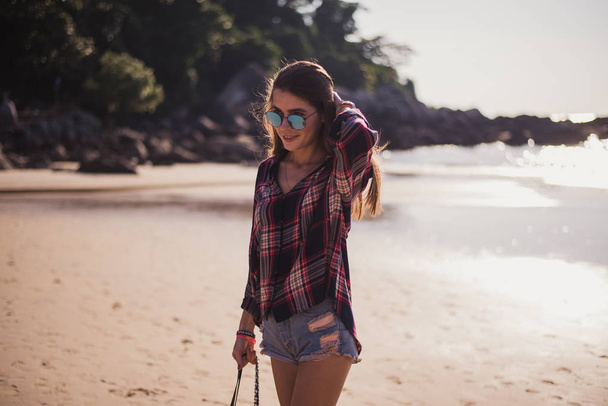 Summer sunny lifestyle fashion portrait of young stylish hipster woman walking on beach,wearing cute trendy outfit, travel, hikes, smiling enjoy her weekends - Фото, зображення
