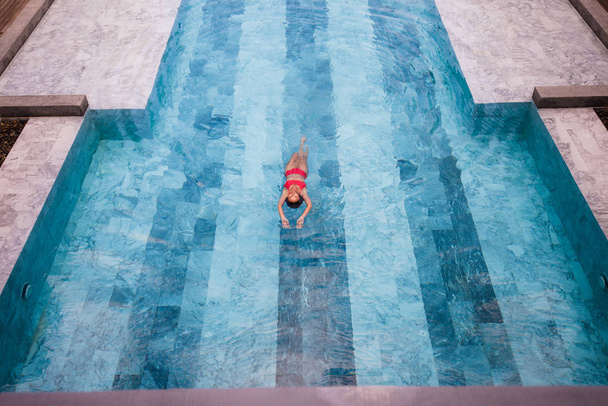 Pohled shora, těší ortofoto svůdné sexy modelu v bílé plavky relaxovat v hotelovém bazénu během její letní víkend. Úžasná móda žena v bikinách s luxusní wellness odpočinek - Fotografie, Obrázek