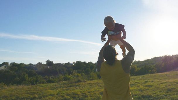 Joven padre jugando con su pequeño hijo al aire libre. Papá criando a su hijo en la naturaleza. Feliz familia pasando tiempo juntos afuera en el prado. Hermoso paisaje de fondo. De cerca.
 - Foto, imagen