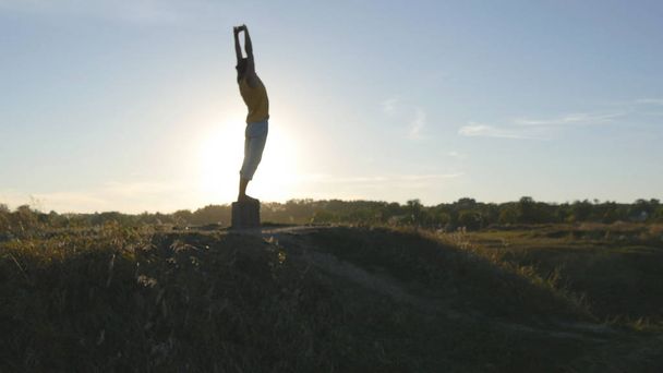 Silhouette of sporty man standing at yoga pose outdoor. Yogi practicing yoga moves and positions in nature. Beautiful sky and sun as background. Healthy active lifestyle - 写真・画像