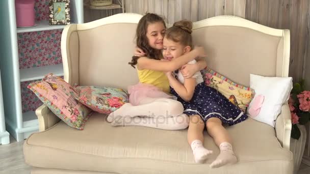 Niña hermana abrazándose sentada en el sofá
 - Metraje, vídeo