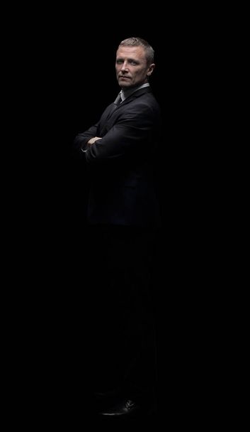 Зрілий бізнесмен в чорному костюмі стоїть і складає руки
 - Фото, зображення