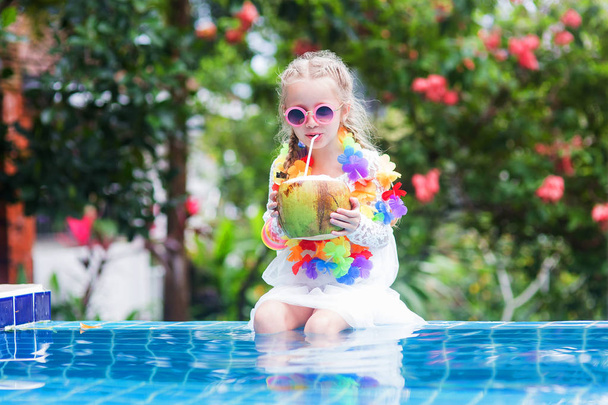 Beautiful girl in pink swimwear and sun glasses is drinking coconut milk, looking at camera and smiling while swimming in the pool - Foto, immagini