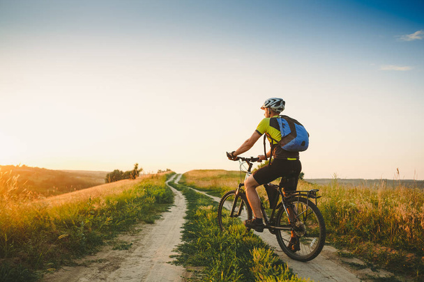 Young man cycling on a rural road through sunset summer meadow - Photo, image