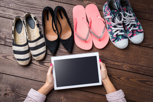 Female shoes collection on wooden table with woman's hands holding white digital tablet - 写真・画像