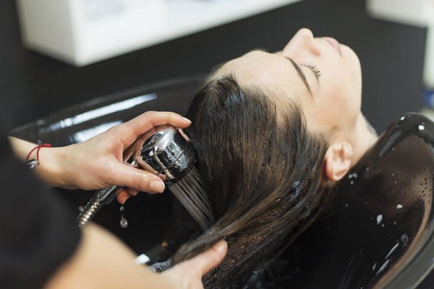 Beautiful young woman with hairdresser washing head at hair salo - Zdjęcie, obraz