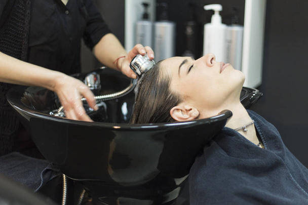 Beautiful young woman with hairdresser washing head at hair salo - Photo, Image