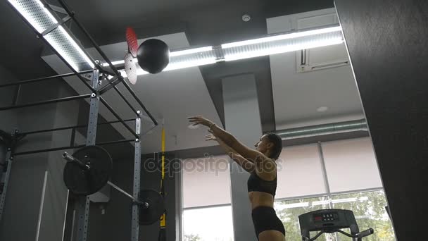 Young strong woman with perfect fitness body in sportswear exercising with medicine ball at gym. Girl doing crossfit training. Female athlete squats during workout indoor. Slow motion. Close up - Video, Çekim