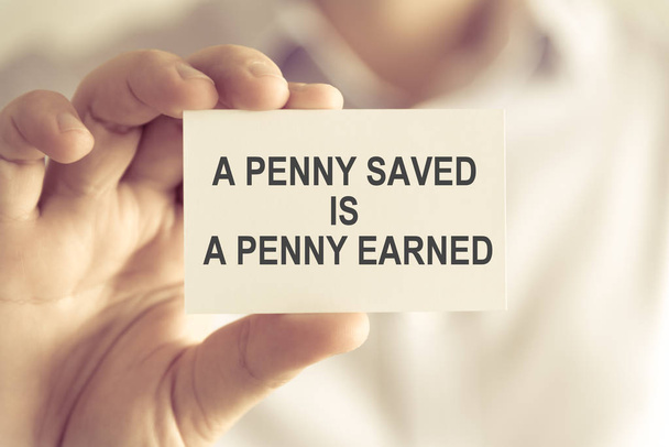 Un uomo d'affari in possesso di un penny risparmiato è un biglietto da messaggio PENNY EARNED
 - Foto, immagini