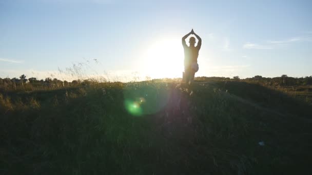 junger Mann, der Yogabewegungen und Positionen am Hügel bei Sonnenuntergang praktiziert. Sportlicher Typ in Yoga-Pose in der Natur. schöne Landschaft als Hintergrund. gesunder aktiver Lebensstil von Yogi im Freien. Zeitlupe - Filmmaterial, Video