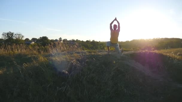 Jeune homme pratiquant des mouvements de yoga et des positions à la colline au coucher du soleil. Homme sportif debout à la pose de yoga dans la nature. Beau paysage comme arrière-plan. Mode de vie sain et actif du yogi en plein air. Mouvement lent
 - Séquence, vidéo