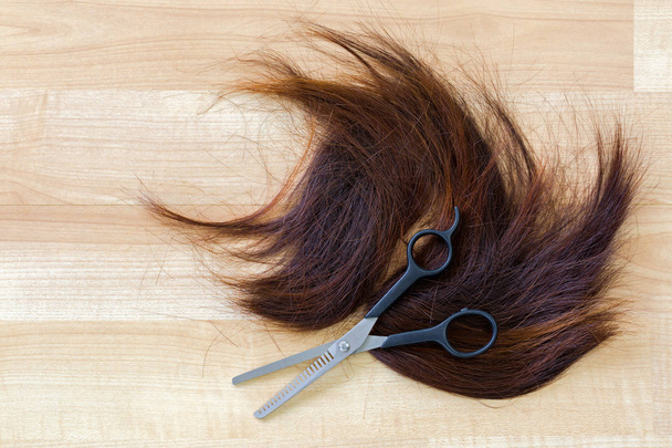 Pair of shears, thinning Scissors on bunch of trimmed cut off reddish brown hair - Фото, изображение