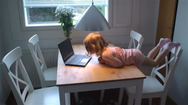 Little girl enthusiastically watching cartoons on the laptop lying on the table. - Πλάνα, βίντεο