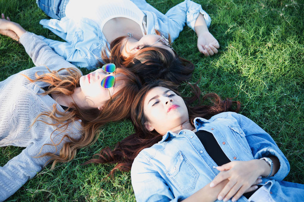 Trois filles asiatiques heureuses allongées sur de l'herbe verte dans des lunettes de soleil
 - Photo, image