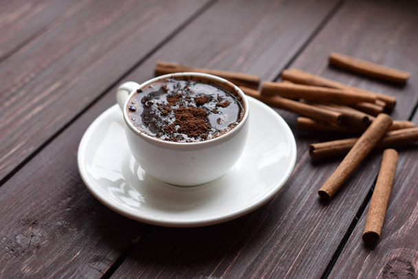 A cup of hot chocolate on a dark wooden surface decorated with cinnamon sticks - Fotoğraf, Görsel