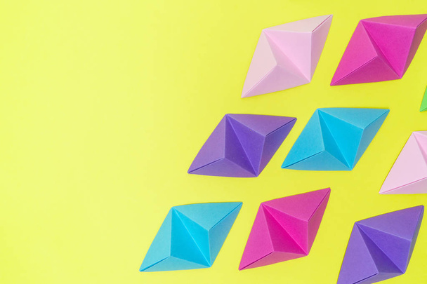 Abstract composition of variable colors origami tetrahedrons on yellow background with copy space on the left side. - Foto, Imagen