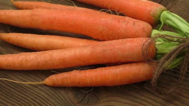 Φρέσκα βιολογικά καρότα με τις πράσινες κορυφές και σπάγγο στο ξύλινο τραπέζι - Πλάνα, βίντεο