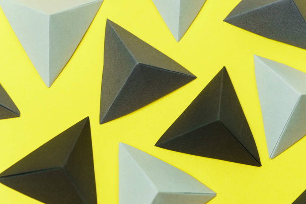 Top view of grey and black origami tetrahedrons on yellow background. - Foto, Bild