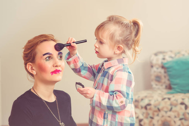 Το χαριτωμένο μικρό κορίτσι κάνουν μακιγιάζ για τη πανέμορφη μητέρα της. Ήπια. - Φωτογραφία, εικόνα