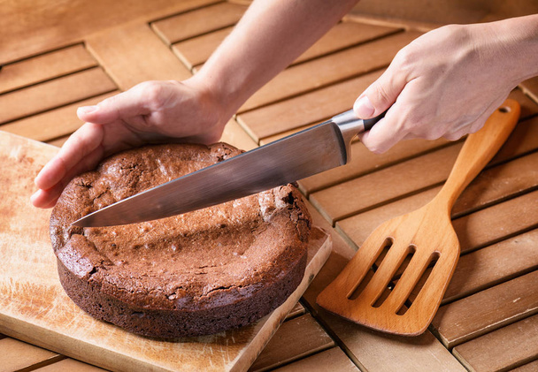 Hand holding knife and cutting freshly baked brownie cake - Fotografie, Obrázek