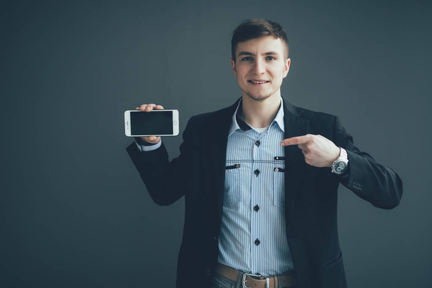 glücklicher Geschäftsmann zeigt mit dem Finger auf leeren Smartphone-Bildschirm vor schwarzem Hintergrund - Foto, Bild