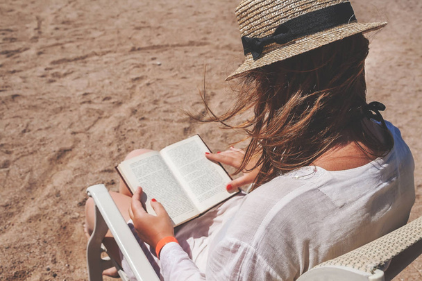 Young adult woman with a hat on the beach reading a book - Foto, immagini