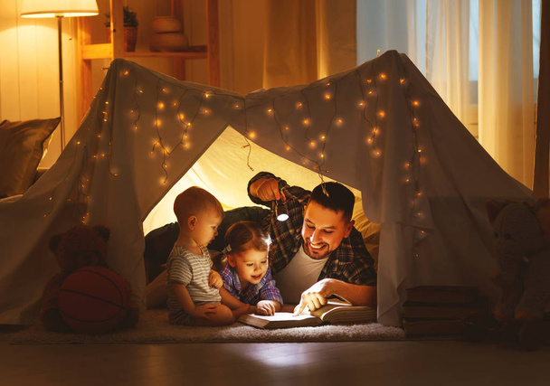 счастливый отец семьи и дети читают книгу в палатке у хома
 - Фото, изображение