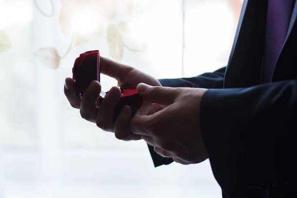 Man makes woman marriage proposal. He opened red jewelry case with engagement ring. He holds box in his hands. - 写真・画像