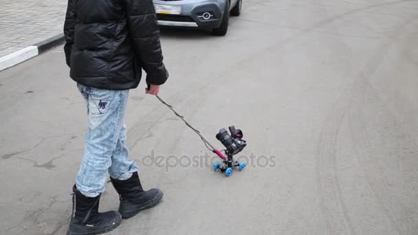 boy with camera on roller on asphalt near cars - Felvétel, videó