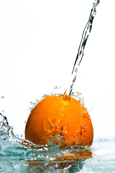 Orange in streams of water on a white background - Фото, изображение