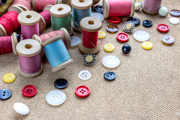 sewing tools (many different colorful thread, needle, many different buttons) on wooden background - Photo, Image