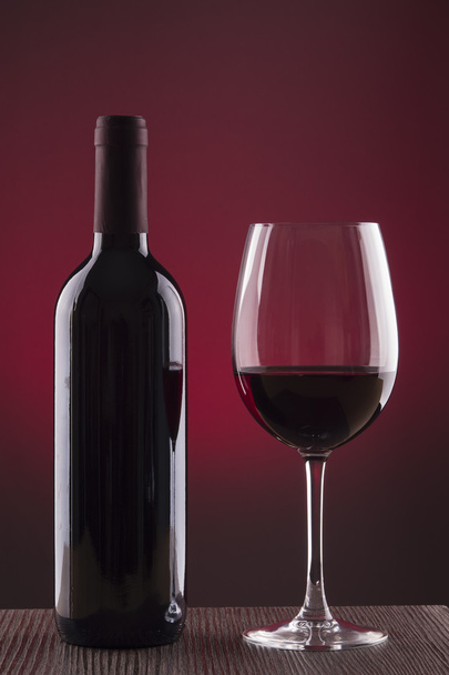 Glass and bottle of wine over red background - Foto, afbeelding