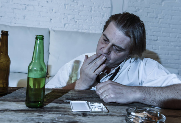 hombre alcohólico y drogadicto desperdiciado con corbata suelta inhalando cocaína y bebiendo botellas de cerveza en casa
  - Foto, Imagen