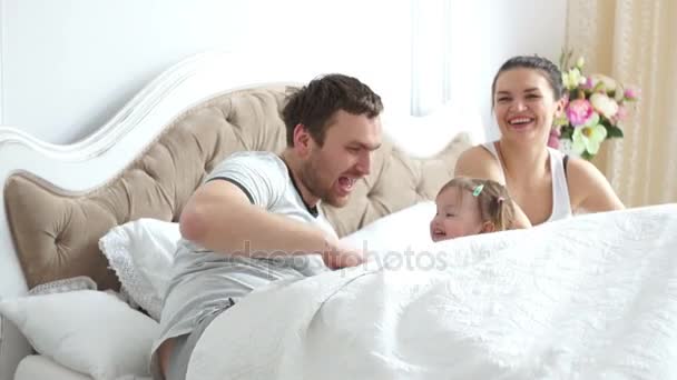 Two parents with a little girl in bed playing and laughing happily - Záběry, video
