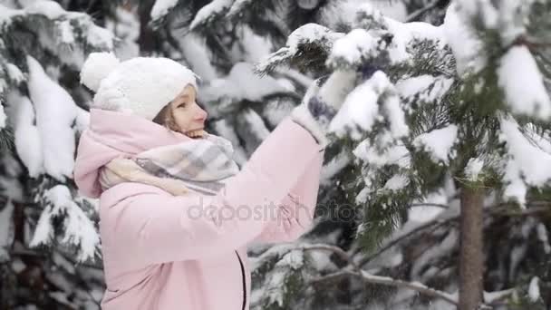 Веселая молодая женщина в зимнем лесу стряхивает снег с еловых ветвей и улыбается замедленным движением
 - Кадры, видео
