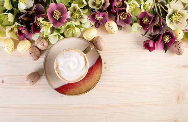 Чашка кофе капучино с весенними цветами и пасхальное яйцо на светлом деревянном фоне. Вид сверху, текстовое пространство
 - Фото, изображение