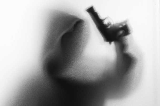 Теневое пятно человека ужаса в куртке с пистолетом-капюшоном в руке.
 - Фото, изображение
