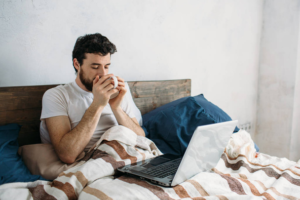 Bearded man lying in morning bed with coffee or tea cup - Foto, imagen