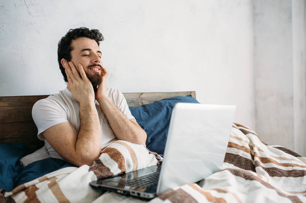 Bearded man lying in morning bed with laptop - Фото, изображение