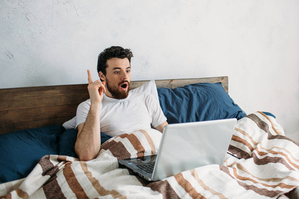 Bearded man lying in morning bed with laptop - Photo, Image