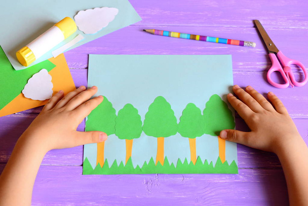 Un niño pequeño hizo una tarjeta de árbol del día de la Tierra. Materiales y herramientas para crear una artesanía infantil sencilla. Los niños tocan el concepto de escritorio del día de la Tierra. Tarjeta de papel idea del día de la Tierra para niños. Actividades de aprendizaje en el jardín de infantes, en casa  - Foto, Imagen