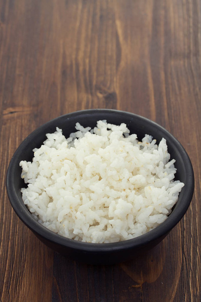 boiled rice in black bowl in wooden background - Fotografie, Obrázek
