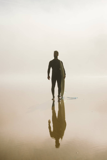 Young man ready for surfing on a misty morning  - Φωτογραφία, εικόνα