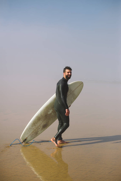Surfer with surfboard at misty beach  - Фото, изображение