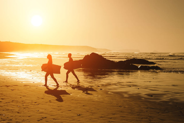 Couple of surfers on a golden sunset at the beach - Photo, image