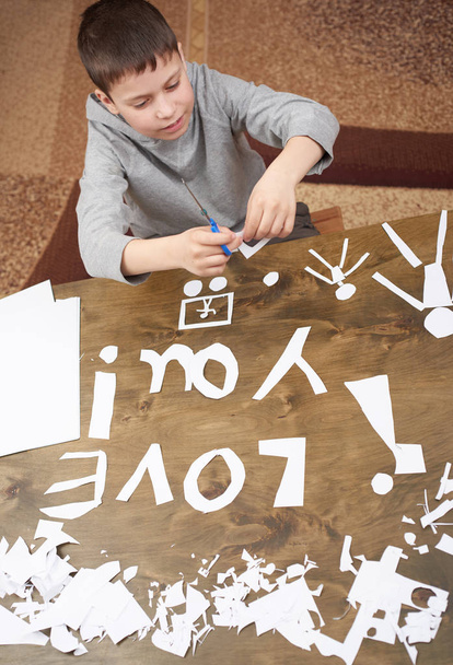 jongen maakt origami - auto en familie, kinderen, ouders, ik hou van je tekst, bovenaanzicht op houten achtergrond - Foto, afbeelding